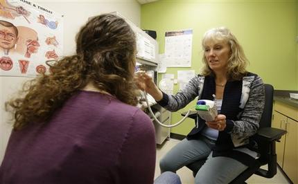 In this Dec. 15, 2014 photo, Stacy Crites, right, a nurse on campus at the University of Washington's Hall Health Primary Care Center in Seattle, takes the temperature of Kandice Joyner, left, a junior studying archeology, during a routine check-up. An unintended side-effect of federal health care reform is leading colleges across the country to transition out of the health insurance business. (AP Photo/Ted S. Warren)