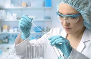 Young female tech or scientist loads liquid sample into test tube with plastic pipette. Shallow DOF, focus on the hand with the tube.