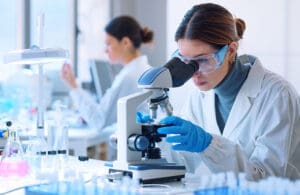 Young scientists conducting research investigations in a medical laboratory, a researcher in the foreground is using a microscope