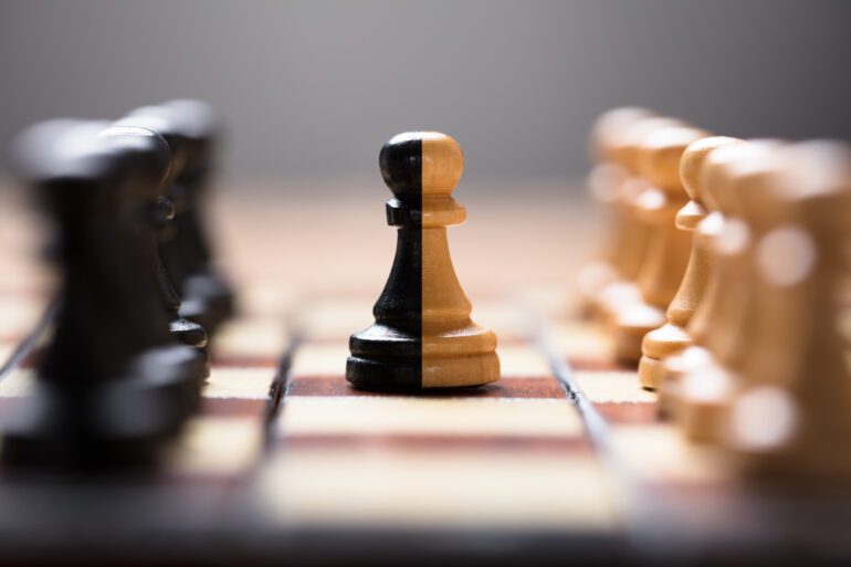 Closeup of double color pawn amidst other chess pieces on board game