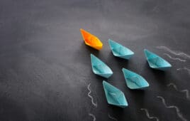 Leadership banner concept with paper boat on blackboard background. One leader ship leads others