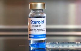 Vial of Steroid injection with a syringe on black table and stainless steel background.