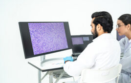 Researchers studying a purple microscopy image of cells on a large screen, digital pathology and histology analysis in bright lab.